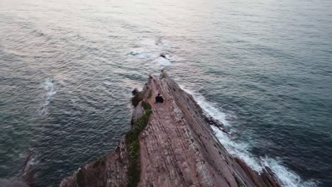 Panoramic-aerial-view-of-a-couple-on-the-cliffs-of-Zumaia,-Spain