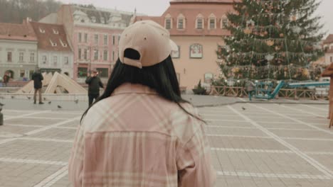 Rückansicht-Einer-Hipster-Frau-Mit-Mütze,-Die-Während-Der-Weihnachtszeit-Auf-Dem-Ratsplatz-In-Brasov,-Rumänien,-Spazieren-Geht