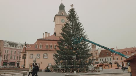 Hombres-Trabajando-En-Una-Plataforma-Elevada-Decorando-Un-Enorme-árbol-De-Navidad-En-La-Plaza-Del-Consejo-En-Brasov,-Rumania