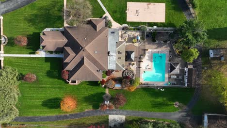 Top-down-aerial-of-large-American-home-with-pool-and-beautiful-landscaping-in-autumn