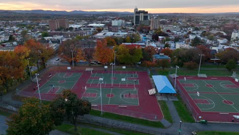 Aerial-truck-shot-of-men-playing-basketball-in-urban-city-park-surrounded-by-colorful-foliage-in-autumn