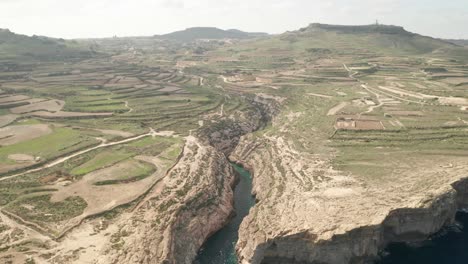 Aerial-tilt-down-reveal-shot-of-the-canyon-Wied-il-Għasri-with-a-beautiful-clear-turquoise-water