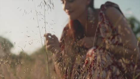A-close-up-slow-motion-shot-of-an-attractive-female-in-a-floral-dress-picking-a-blade-of-grass-from-the-ground-before-putting-it-in-her-mouth-as-she-appreciates-the-beauty-of-nature-outdoors,-India