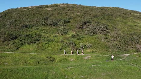 Group-of-friends-walking-in-a-line-up-a-green-hill
