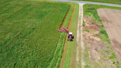 Circling-Drone-Shot-of-Red-Tractor-in-Farm-Field-Harvesting-Hay
