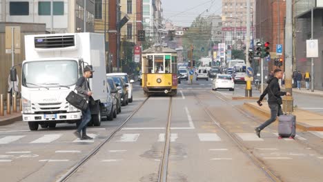 People-walk-on-crosswalk-with-cars-and-tramway-in-background,-Milan-city-center