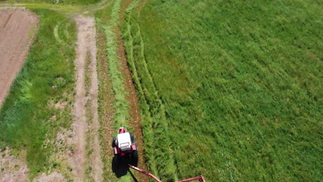 Drone-Shot-of-Tractor-Harvesting-Farm-Field-of-Green-Hay-on-a-Sunny-Day