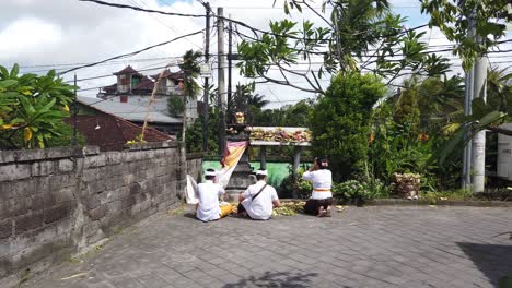 Familia-Hindú-Balinesa-Rezando-En-Un-Templo-Callejero-En-Gianyar,-Sukawati,-Bali,-Indonesia,-Levantando-Sus-Manos-Frente-A-Las-Ofrendas