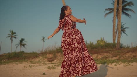 A-carefree-Caucasian-female-twirling-around-dancing-on-a-beach-wearing-a-red-floral-summers-dress-on-a-beautiful-sunny-day-outdoors,-India