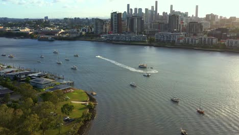 Aerial-view-tilt-up-shot-capturing-Newstead-river-terrace,-waterfront-residential-apartment-complex-along-Brisbane-river-with-downtown-cityscape-on-the-skyline-at-sunset,-capital-city-of-Queensland