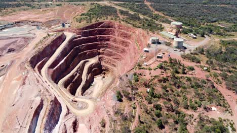 Aerial-drone-mining-pit-open-cut-copper-ore-mine-with-water-tank-bushland-red-rock-travel-industry-tourism-Fort-Bourke-Hill-Cobar-NSW-Australia-outback-4K