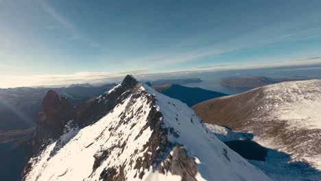 Vuelo-Fpv-A-Lo-Largo-De-Los-Picos-Nevados-De-La-Cordillera-En-Noruega-Durante-El-Frío-Día-De-Invierno-Con-Luz-Solar---Océano-En-Segundo-Plano