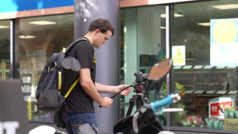 Young-caucasian-man-with-a-camera-on-a-tripod-is-walking-and-setting-up-on-the-streets-of-London-during-late-summer-by-himself