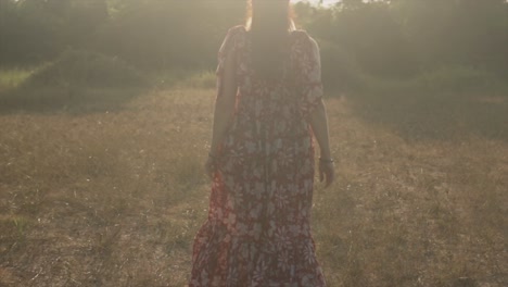 A-slow-motion-shot-of-the-back-of-a-Caucasian-female-wearing-a-floral-dress-feeling-free,-running-through-a-field-towards-the-morning-sunrise-on-a-beautiful-day-outdoors,-India