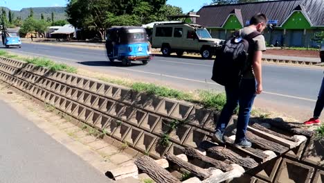 Full-shot-of-man-crossing-a-wooden-handmade-bridge-in-Arusha-Tanzania,-busy-road