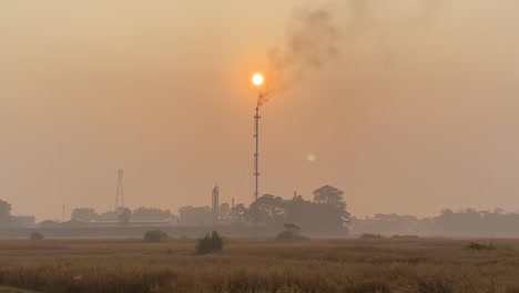 Establisher-wide-shot-of-hazy-sunset-with-Gas-Tower-Plant-burning,-fumes-release