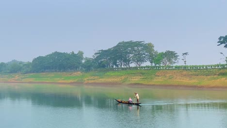 Telephoto-shot-of-fisherman-stirring-boat-while-woman-is-sitting-down,-Sylhet
