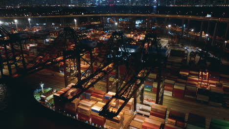 Portalkräne,-Die-Auf-Einem-Containerschiff-Arbeiten,-Während-Der-Verkehr-über-Die-Hohe-Brücke-Im-Hintergrund-Fährt,-Mit-Blick-Auf-Die-Skyline-Von-Hongkong