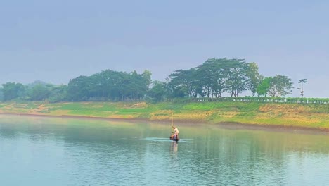 Two-people-on-board-of-traditional-Asian-fishing-boat-crossing-Surma-river,-Sylhet