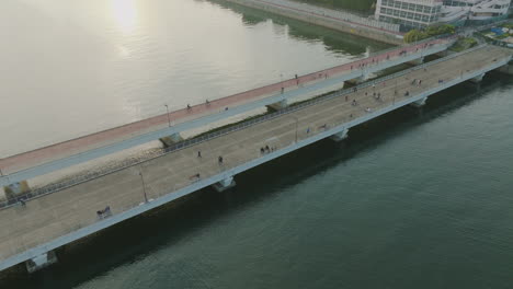 Schöne-Kreisförmige-Aufnahme-Einer-Brücke-über-Einen-Fluss-Mit-Menschen-Und-Fahrrädern-Darüber