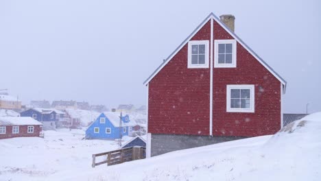 Red-house-in-a-snowstorm-with-other-houses-behind-in-Ilulissat,-Greenland