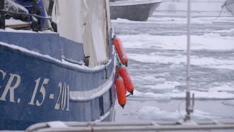 Zeitlupenvideo-Von-Orangefarbenen-Tenderbooten-Auf-Einem-Boot-Im-Schneesturm,-Das-In-Einem-Zugefrorenen-Hafen-In-Grönland-Festgemacht-Ist