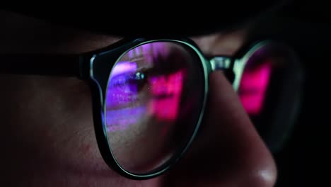 Man-on-his-computer-at-night-ultra-violet-blue-light-hitting-glasses---closeup-handheld-shot