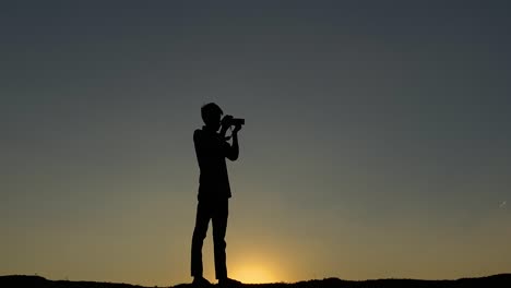 Silhouette-of-photograher-with-camera-taking-pictures-at-sunset-sky,-zoom-in