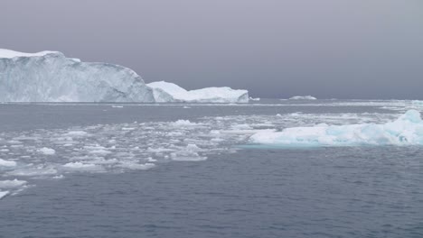 Schwenken-Sie-In-Zeitlupe-über-Kleine-Eisschollen-Und-Große-Eisberge,-Die-An-Einem-Bewölkten-Tag-Im-Meer-Schwimmen