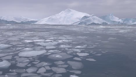 Zeitlupenvideo-Eines-Großen-Eisbergs-Und-Kleinerer-Eisschollen-Im-Vordergrund-Vor-Der-Küste-Grönlands