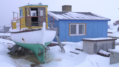 Video-En-Cámara-Lenta-De-Un-Barco-De-Pesca-Amarillo-Fuera-De-Una-Casa-Azul-En-Una-Tormenta-De-Nieve-En-Ilulissat,-Groenlandia