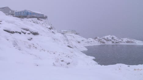 Slow-motion-video-of-two-houses-on-the-snowy-arctic-hill-coast-in-a-snowstorm-in-Ilulissat,-Greenland