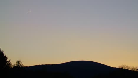 Plane-Flying-in-Distance-over-Mountain-at-Sunset