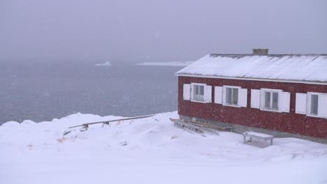 Zeitlupenvideo-Eines-Roten-Bootshauses-An-Der-Arktischen-Küste-In-Einem-Schneesturm-Mit-Kanus-Und-Eisbergen
