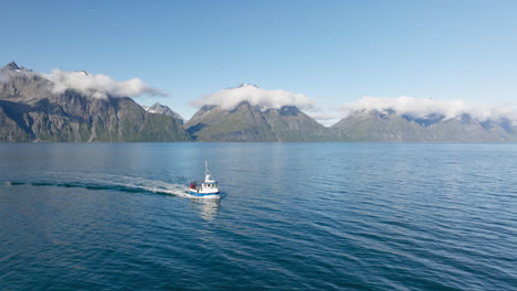 People-on-board-of-fishing-boat-sailing-in-Lyngen-fjord-with-rocky-mountains-of-Lyngen-Alps-in-background-on-sunny-day,-Norway