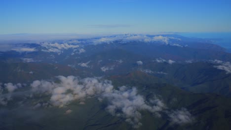 Eine-Luftperspektive-Von-Wolken,-Die-Tagsüber-über-Einer-Grünen,-Bergigen-Landschaft-Schweben