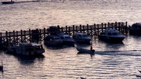 Solo-fisherman-person-in-motorboat-at-twilight-sunset-coming-into-dock-to-moor-in-fishing-village-of-Labuan-Bajo-on-Flores-Island,-Nusa-Tenggara-region-of-east-Indonesia