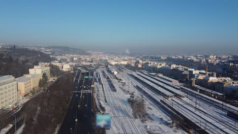 Autoverkehr-Entlang-Des-Bahnhofs-Prag-Smichov,-Luftdrohne-Winteransicht,-Stadt-Im-Hintergrund,-Tschechische-Republik