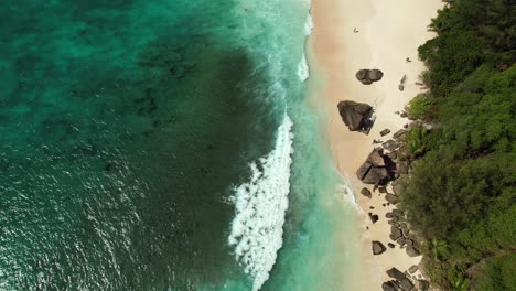 Mahe-Seychellen-Drohnenaufnahme-Von-Kunden,-Die-Am-Strand-In-Der-Nähe-Von-Granitfelsen-Spazieren-Gehen,-Sonniger-Tag,-Türkisfarbenes-Wasser