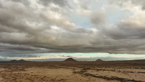 Mojave-wüste-Und-Ferne-Buttes-Mit-Der-Winzigen-Silhouette-Eines-Einsamen-Menschen,-Der-In-Der-Weiten-Landschaft-Spaziert---Aufsteigende-Luftaufnahme