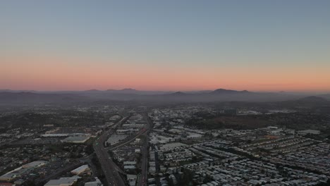A-panning-drone-shot-captures-a-beautiful-sunset-over-the-city,-with-the-moon-visible-in-the-distance