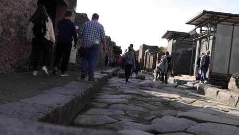 People-walking-on-brick-path-in-Pompeii,-Italy-with-stable-establishing-shot