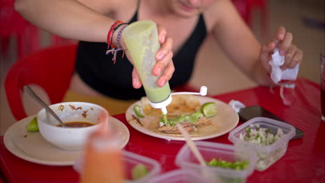 Cierre-En-Cámara-Lenta-De-Una-Mujer-Latina-Preparando-Su-Taco-De-Barbacoa-Con-Salsa-De-Chile-Verde-En-Un-Restaurante-En-México