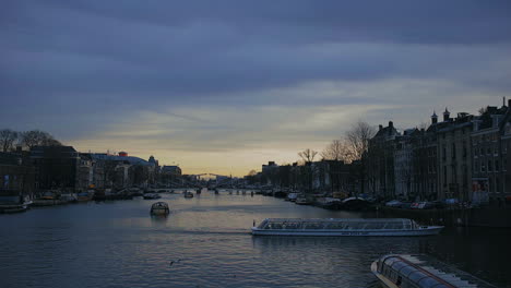 Amsterdam-Amstel-river,-sunset-on-January-2023,-tourist-boat-passing-by