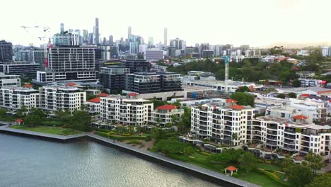 Cinematic-aerial-view-fly-around-Newstead-river-terrace,-waterfront-residential-apartment-complex-along-Brisbane-river-with-downtown-cityscape-on-the-skyline-at-sunset,-capital-city-of-Queensland