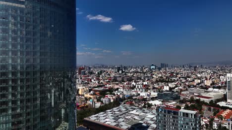 Aerial-view-near-the-Mitikah-building,-overlooking-the-cityscape-of-sunny-Benito-Juarez,-Mexico-city---ascending,-drone-shot