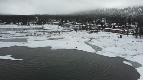 Aerial-View-of-People-on-Snow-Capped-Coast-of-Big-Bear-Lake-on-Cold-Winter-Day,-California-USA,-Drone-Shot