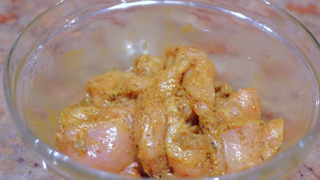 Close-up-shot-of-Marinated-chicken-with-various-spices-in-a-glass-bowl-on-a-marble-table