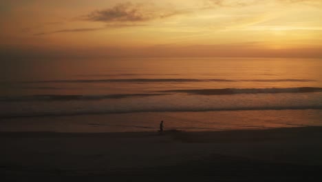 Aerial,-silhouette-of-person-running-on-the-beach-early-in-the-morning-during-golden-hour