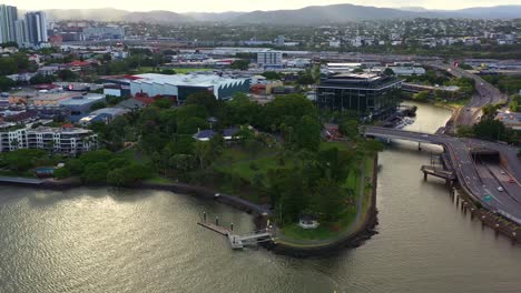 Cinematic-aerial-panning-view-along-the-northern-river-shore-capturing-breakfast-creek-and-waterfront-residential-apartment-complex-in-Newstead-inner-city-suburb-at-sunset,-Brisbane,-Queensland